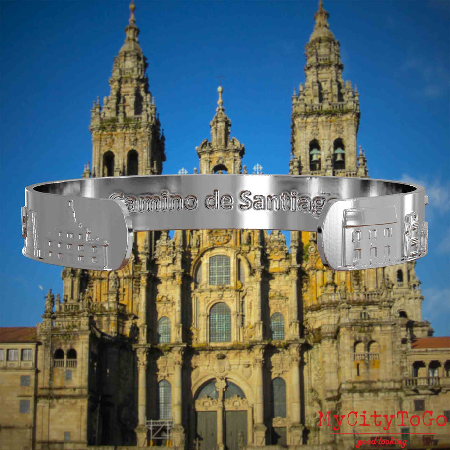Innenseite eines silbernen Armreifs mit Reliefs bekannter Sehenswürdigkeiten und Elemente des Jakobsweges und der Gravur Camino de Santiago. Den Hintergrund bildet die Kathedrale von Santiago de Compostela.