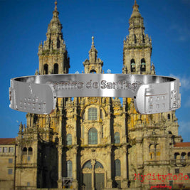 Innenseite eines silbernen Armreifs mit Reliefs bekannter Sehenswürdigkeiten und Elemente des Jakobsweges und der Gravur Camino de Santiago. Den Hintergrund bildet die Kathedrale von Santiago de Compostela.