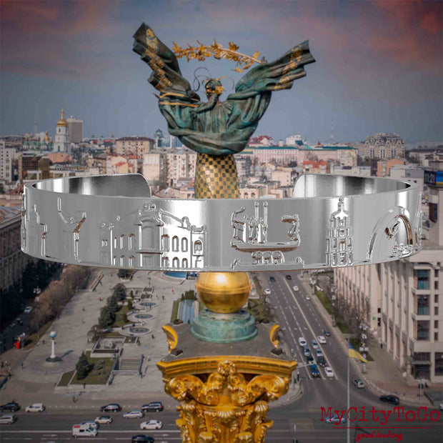 Versilberter Armreif mit Reliefs bekannter Sehenswürdigkeiten der Stadt Kiew. Den Hintergrund bildet eine Ansicht der Stadt Kiew.