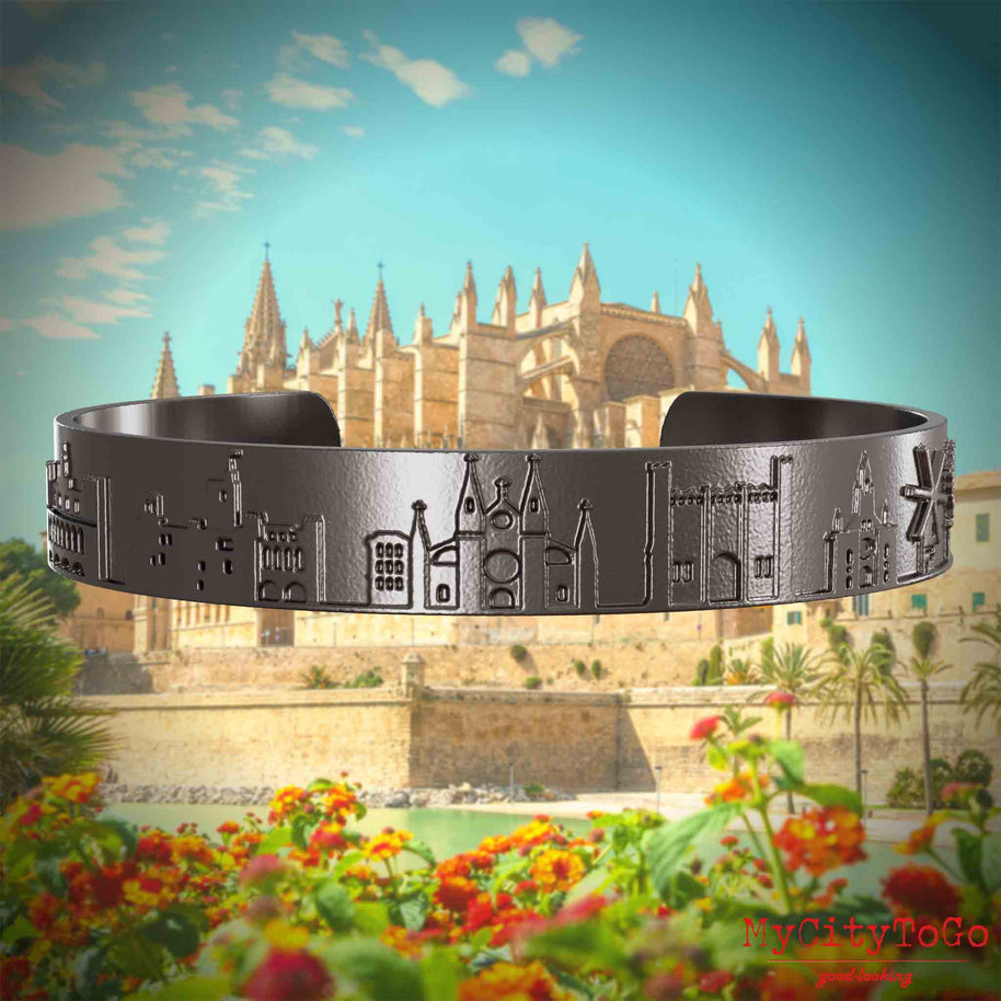 Armreif aus Titan mit Reliefs bekannter Sehenswürdigkeiten der Stadt Palma de Mallorca. Den Hintergrund bildet eine Ansicht der Stadt Palma de Mallorca.