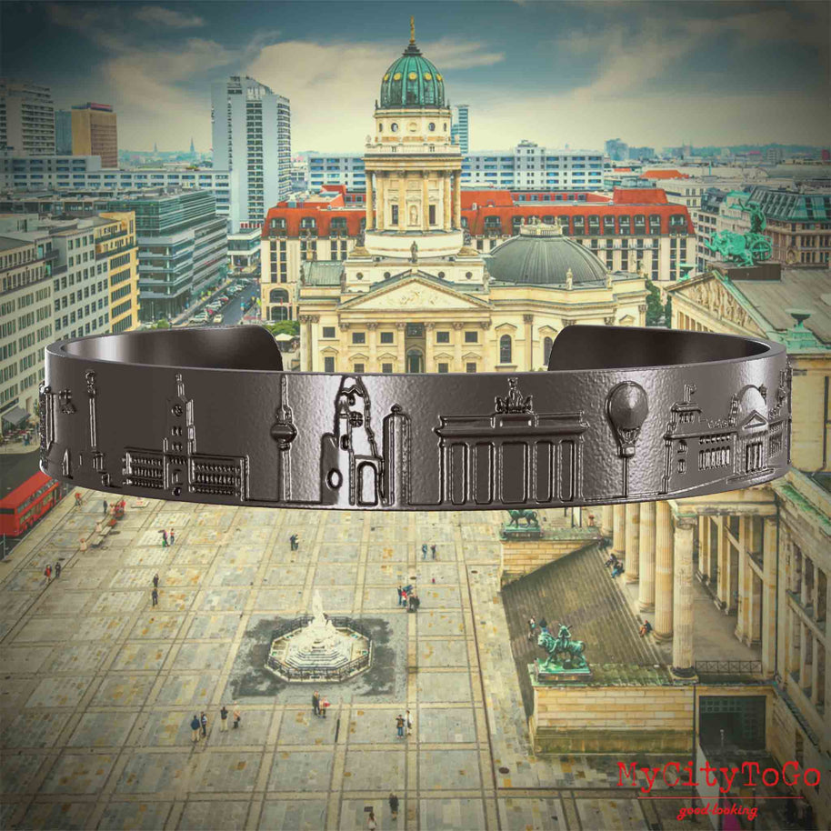 Armreif aus Titan mit Reliefs bekannter Sehenswürdigkeiten der Stadt Berlin. Den Hintergrund bildet eine Ansicht der Stadt Berlin. 