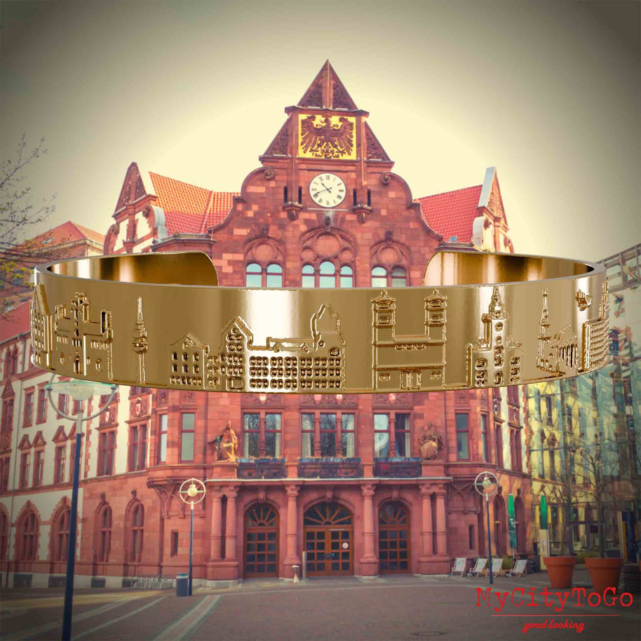 Vergoldeter Armreif mit Reliefs bekannter Sehenswürdigkeiten der Stadt Dortmund. Den Hintergrund bildet eine Ansicht der Stadt Dortmund.