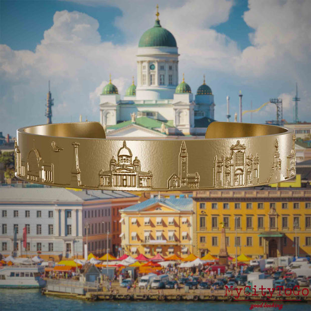 Armreif aus vergoldetem Edelstahl mit Reliefs bekannter Sehenswürdigkeiten der Stadt Helsinki. Den Hintergrund bildet eine Ansicht der Stadt Helsinki.