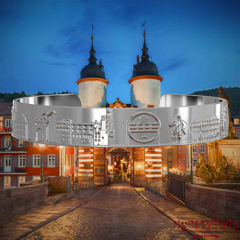Versilberter Armreif mit Reliefs bekannter Sehenswürdigkeiten der Stadt Heidelberg. Den Hintergrund bildet eine Ansicht der Stadt Heidelberg.