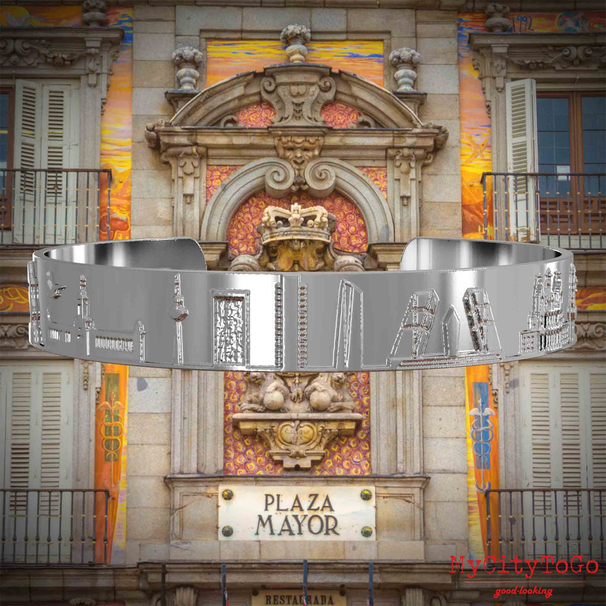 Versilberter Armreif mit Reliefs bekannter Sehenswürdigkeiten der Stadt Madird. Den Hintergrund bildet eine Ansicht der Stadt Madrid.