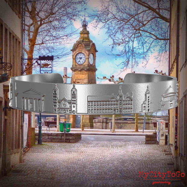 Armreif aus Edelstahl mit Reliefs bekannter Sehenswürdigkeiten der Stadt Duesseldorf. Den Hintergrund bildet eine Ansicht der Stadt Duesseldorf.