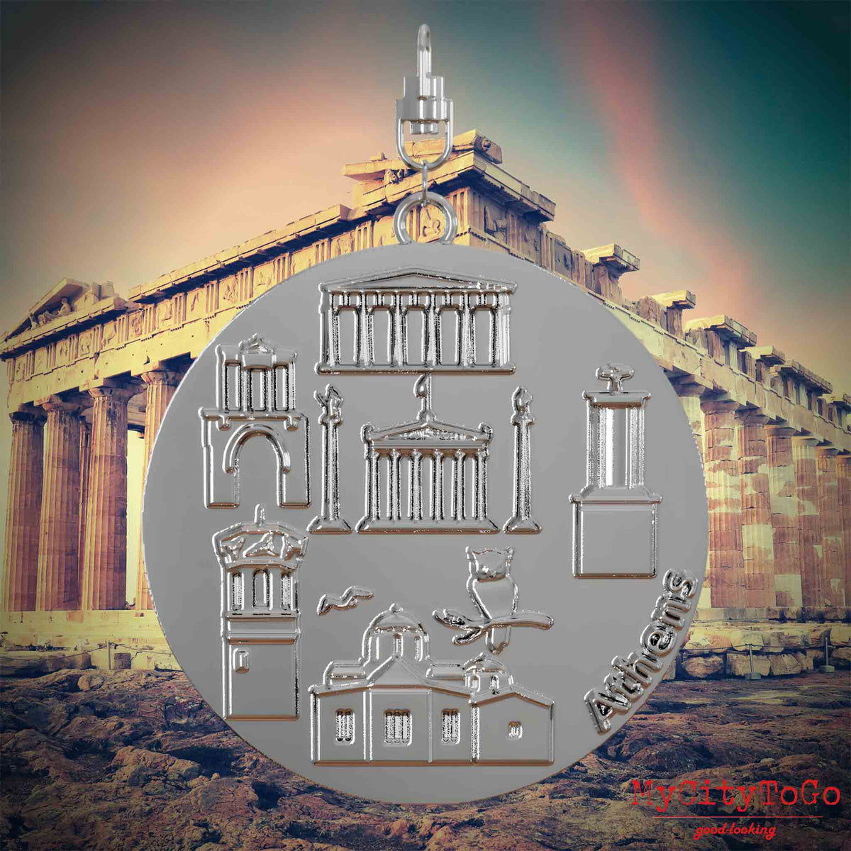 Halskette mit Drehwirbel und Rückseite eines silbernen Schmuckanhängers, auf dem Reliefs bekannter Sehenswürdigkeiten der Stadt Athen abgebildet sind. Den Hintergrund bildet eine Ansicht der Stadt Athen.
