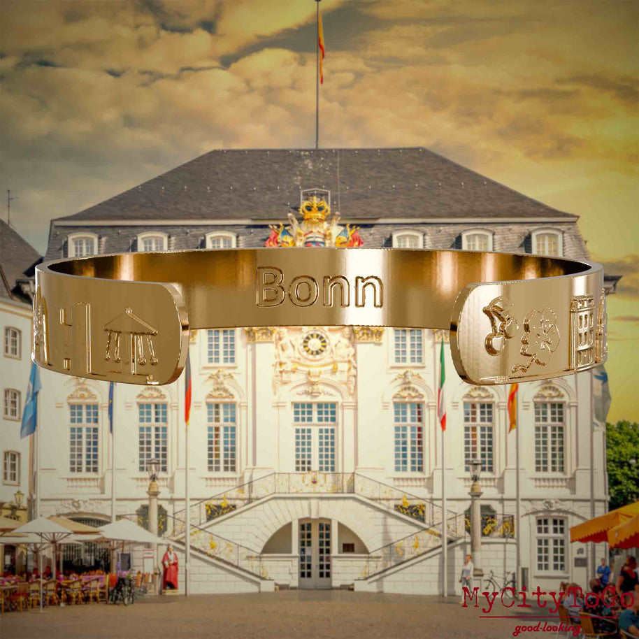 Innenseite eines vergoldeten Armreifs mit Reliefs bekannter Sehenswürdigkeiten der Stadt Bonn und einer Gravur des Stadtnamens. Den Hintergrund bildet eine Ansicht der Stadt Bonn.