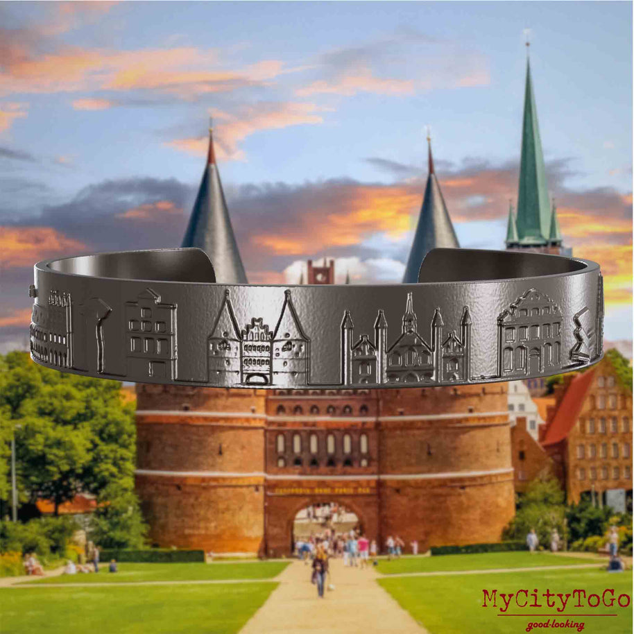 Armreif aus Titan mit Reliefs bekannter Sehenswürdigkeiten der Stadt Luebeck. Den Hintergrund bildet eine Ansicht der Stadt Luebeck.