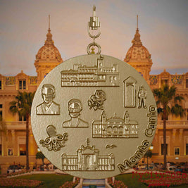 Halskette mit Drehwirbel und Rückseite eines Schmuckanhängers aus vergoldetem Edelstahl, auf dem Reliefs bekannter Sehenswürdigkeiten der Stadt Monte Carlo abgebildet sind. Den Hintergrund bildet eine Ansicht der Stadt Monte Carlo.
