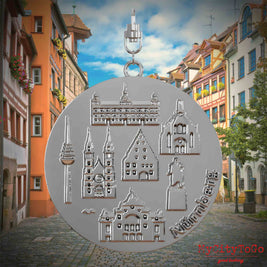 Halskette mit Drehwirbel und Vorderseite eines silbernen Schmuckanhängers, auf dem Reliefs bekannter Sehenswürdigkeiten der Stadt Nürnberg abgebildet sind. Den Hintergrund bildet eine Ansicht der Stadt Nürnberg.