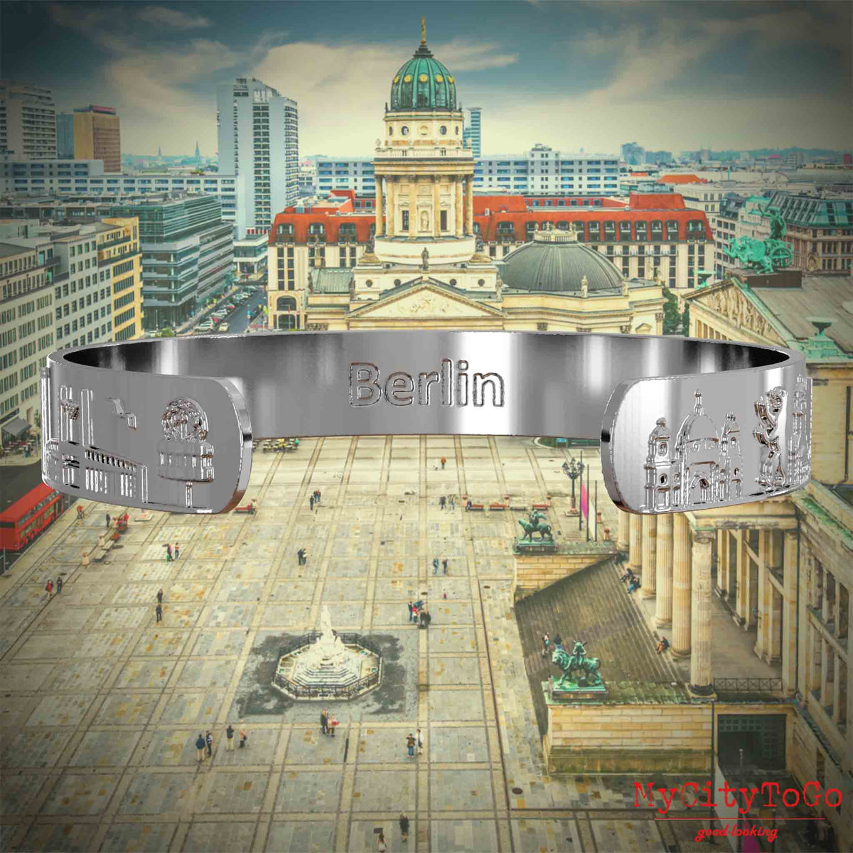 Innenseite eines silbernen Armreifs mit Reliefs bekannter Sehenswürdigkeiten der Stadt Berlin und einer Gravur des Stadtnamens. Den Hintergrund bildet eine Ansicht der Stadt Berlin. 