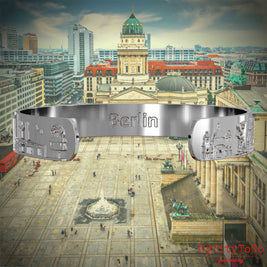 Innenseite eines silbernen Armreifs mit Reliefs bekannter Sehenswürdigkeiten der Stadt Berlin und einer Gravur des Stadtnamens. Den Hintergrund bildet eine Ansicht der Stadt Berlin. 