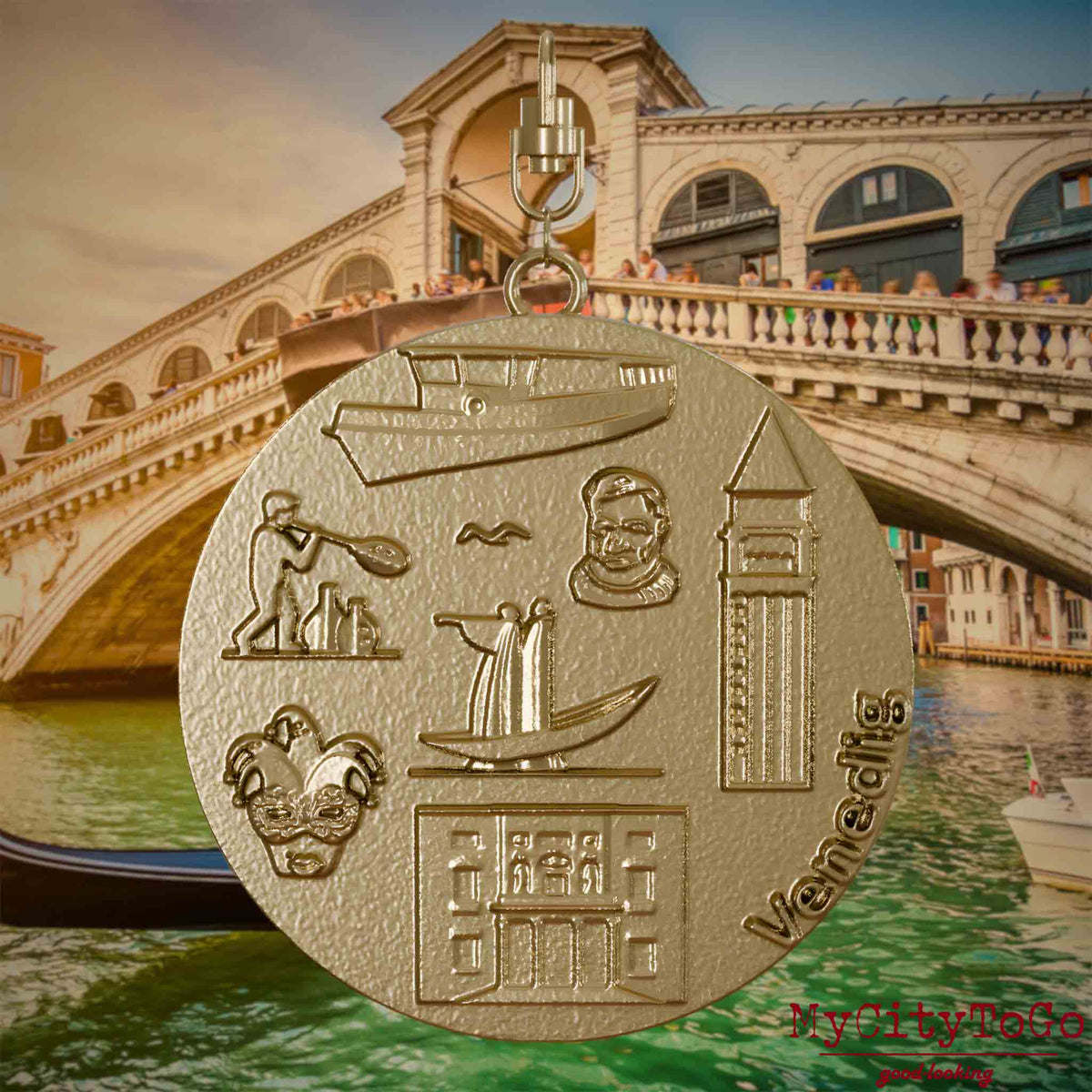 Halskette mit Drehwirbel und Rückseite eines Schmuckanhängers aus vergoldetem Edelstahl, auf dem Reliefs bekannter Sehenswürdigkeiten der Stadt Venedig abgebildet sind. Den Hintergrund bildet eine Ansicht der Stadt Venedig.
