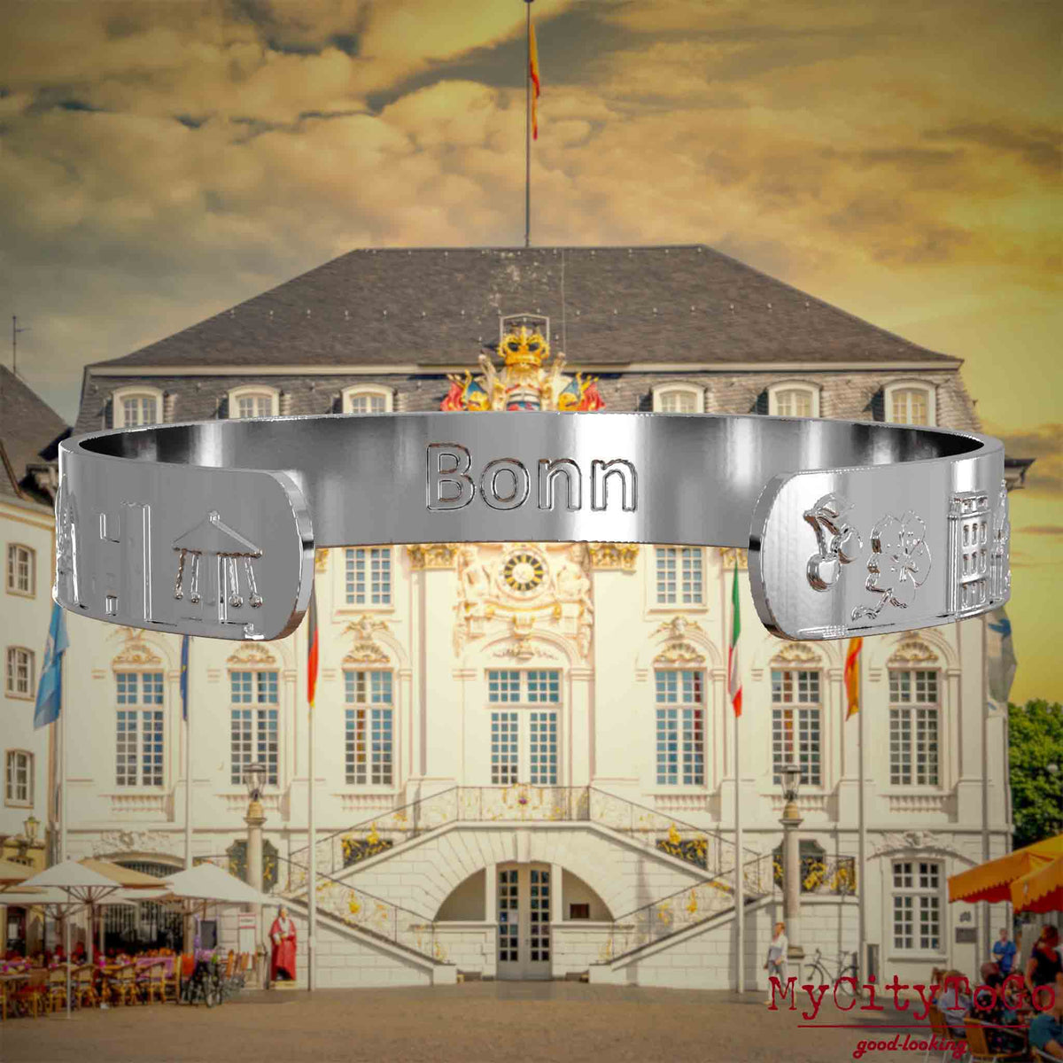 Innenseite eines silbernen Armreifs mit Reliefs bekannter Sehenswürdigkeiten der Stadt Bonn und einer Gravur des Stadtnamens. Den Hintergrund bildet eine Ansicht der Stadt Bonn.