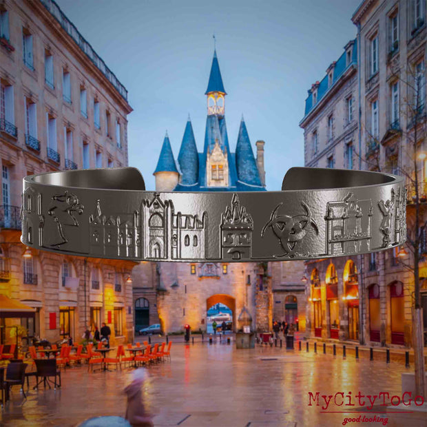 Armreif aus Titan mit Reliefs bekannter Sehenswürdigkeiten der Stadt Bordeaux. Den Hintergrund bildet eine Ansicht der Stadt Bordeaux.
