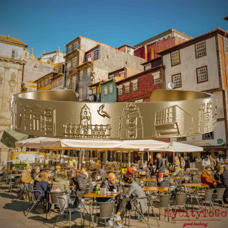 Armreif aus vergoldetem Edelstahl mit Reliefs bekannter Sehenswürdigkeiten der Stadt Porto. Den Hintergrund bildet eine Ansicht der Stadt Porto.