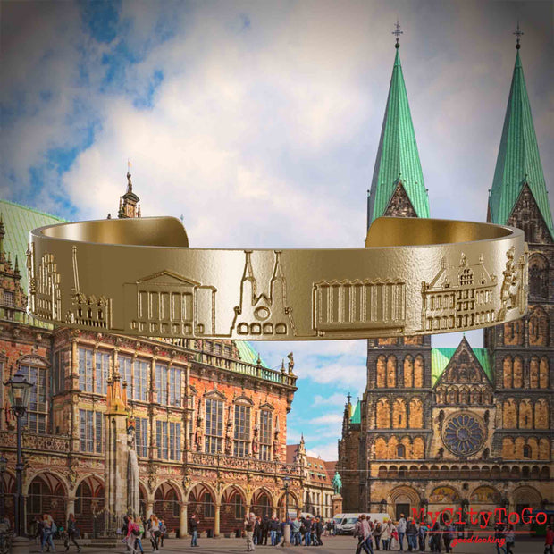 Armreif aus vergoldetem Edelstahl mit Reliefs bekannter Sehenswürdigkeiten der Stadt Bremen. Den Hintergrund bildet eine Ansicht der Stadt Bremen.
