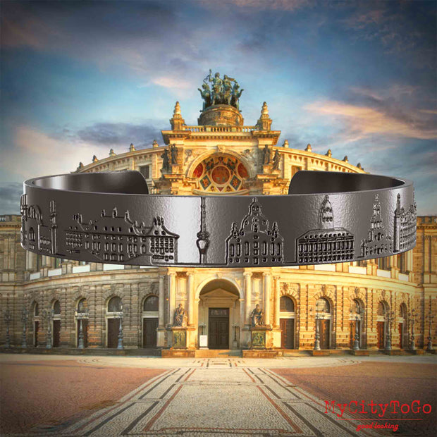 Armreif aus Titan mit Reliefs bekannter Sehenswürdigkeiten der Stadt Dresden. Den Hintergrund bildet eine Ansicht der Stadt Dresden.