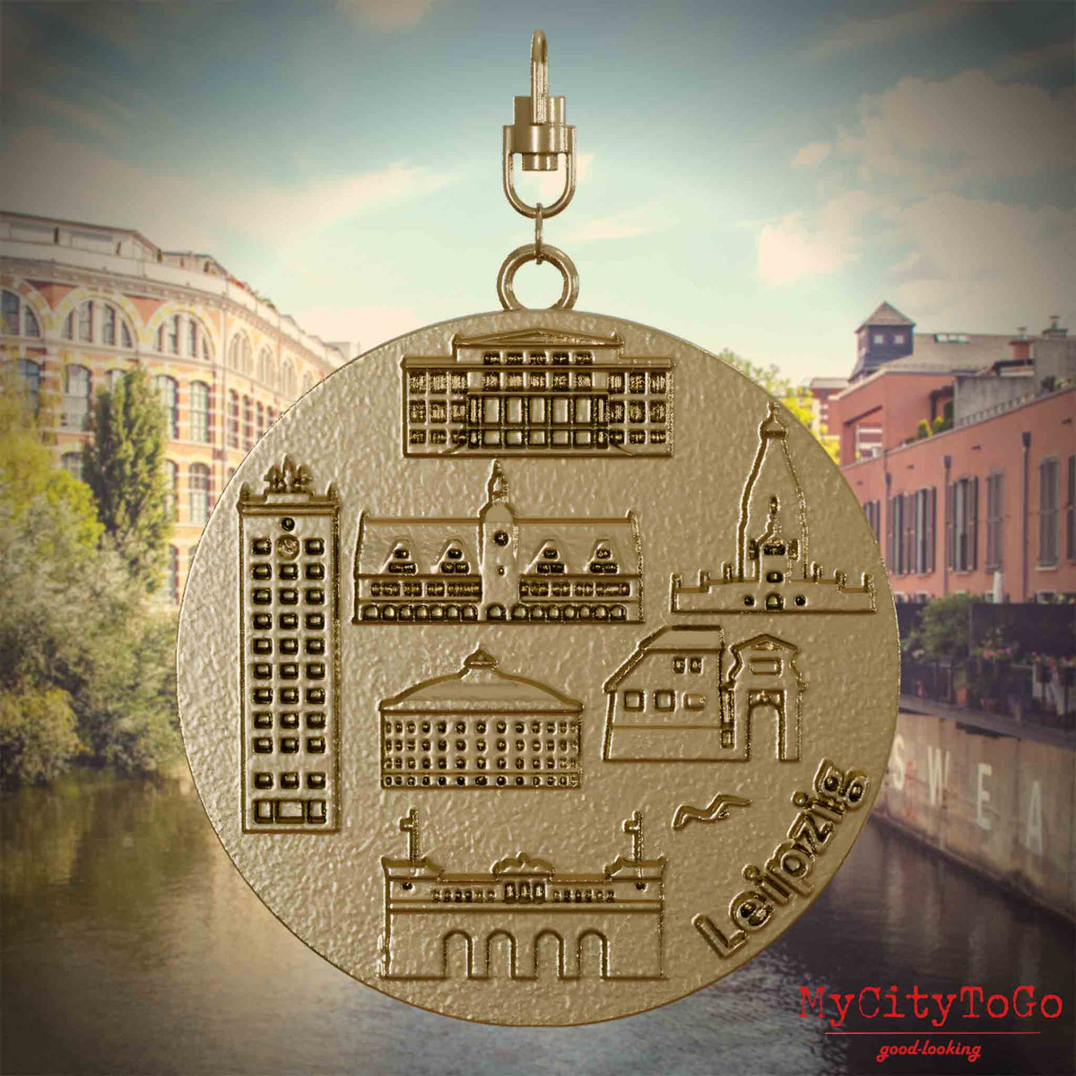 Halskette mit Drehwirbel und Rückseite eines Schmuckanhängers aus vergoldetem Edelstahl, auf dem Reliefs bekannter Sehenswürdigkeiten der Stadt Leipzig abgebildet sind. Den Hintergrund bildet eine Ansicht der Stadt Leipzig.