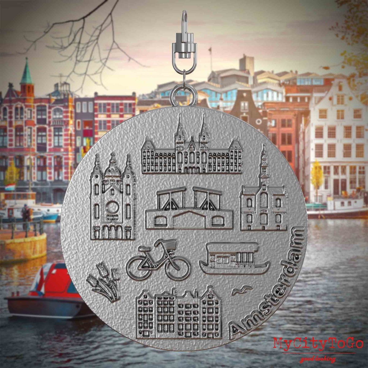 Halskette mit Drehwirbel und Vorderseite eines Schmuckanhängers aus Edelstahl, auf dem Reliefs bekannter Sehenswürdigkeiten der Stadt Amsterdam abgebildet sind. Den Hintergrund bildet eine Ansicht der Stadt Amsterdam.
