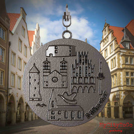 Halskette mit Drehwirbel und Vorderseite eines Schmuckanhängers aus Titan, auf dem Reliefs bekannter Sehenswürdigkeiten der Stadt Muenster abgebildet sind. Den Hintergrund bildet eine Ansicht der Stadt Muenster.