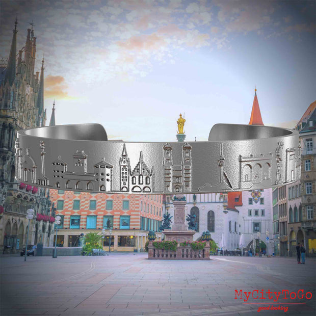 Armreif aus Edelstahl mit Reliefs bekannter Sehenswürdigkeiten der Stadt München. Den Hintergrund bildet eine Ansicht der Stadt Muenchen.