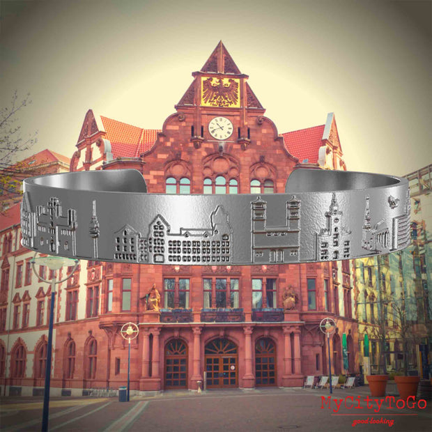 Armreif aus Edelstahl mit Reliefs bekannter Sehenswürdigkeiten der Stadt Dortmund. Den Hintergrund bildet eine Ansicht der Stadt Dortmund.