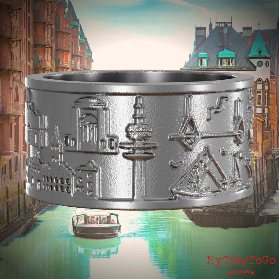 Ring aus Edelstahl mit Reliefs bekannter Sehenswürdigkeiten der Stadt Hamburg. Den Hintergrund bildet eine Ansicht der Stadt Hamburg.