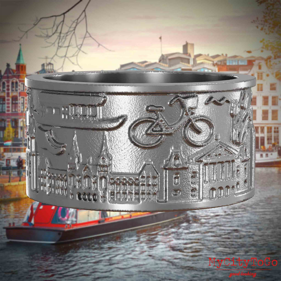 Ring aus Edelstahl mit Reliefs bekannter Sehenswürdigkeiten der Stadt Amsterdam. Den Hintergrund bildet eine Ansicht der Stadt Amsterdam.