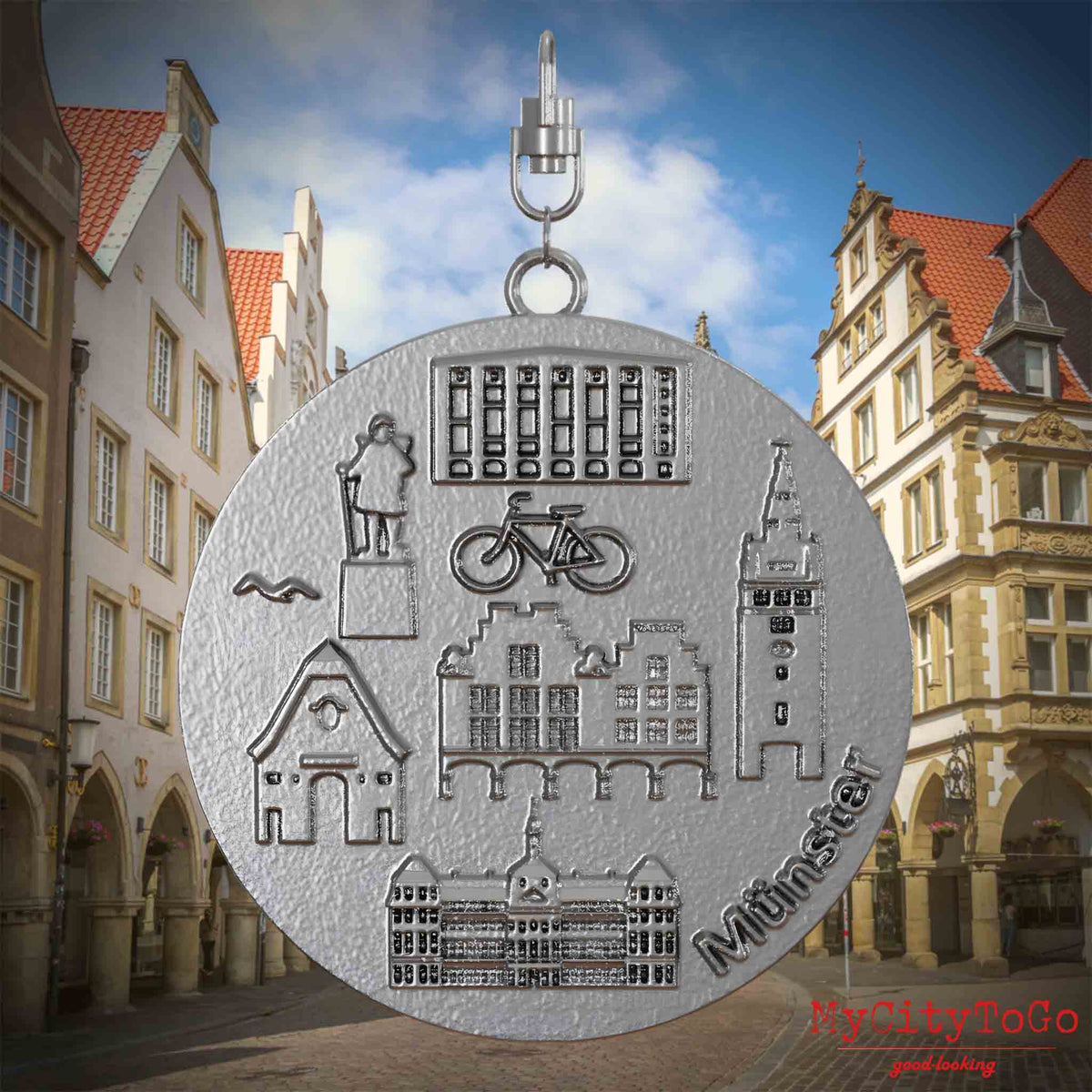 Halskette mit Drehwirbel und Rückseite eines Schmuckanhängers aus Edelstahl, auf dem Reliefs bekannter Sehenswürdigkeiten der Stadt Muenster abgebildet sind. Den Hintergrund bildet eine Ansicht der Stadt Muenster.