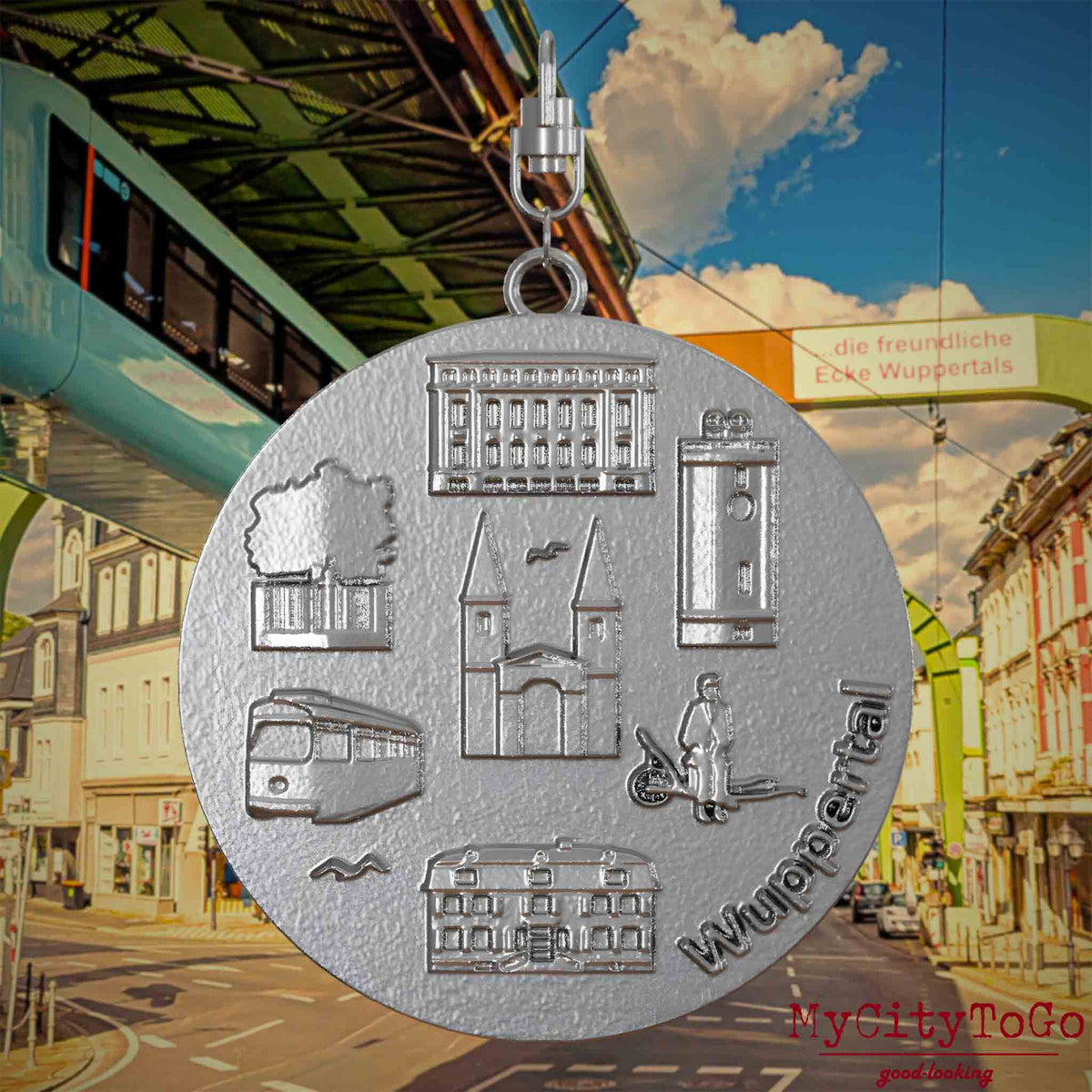 Halskette mit Drehwirbel und Rückseite eines Schmuckanhängers aus Edelstahl, auf dem Reliefs bekannter Sehenswürdigkeiten der Stadt Wuppertal abgebildet sind. Den Hintergrund bildet eine Ansicht der Stadt Wuppertal.
