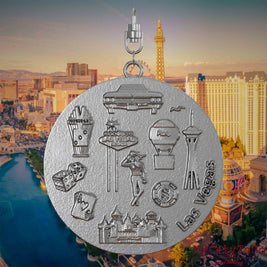 Halskette mit Drehwirbel und Rückseite eines Schmuckanhängers aus Edelstahl, auf dem Reliefs bekannter Sehenswürdigkeiten der Stadt Las Vegas abgebildet sind. Den Hintergrund bildet eine Ansicht der Stadt Las Vegas.