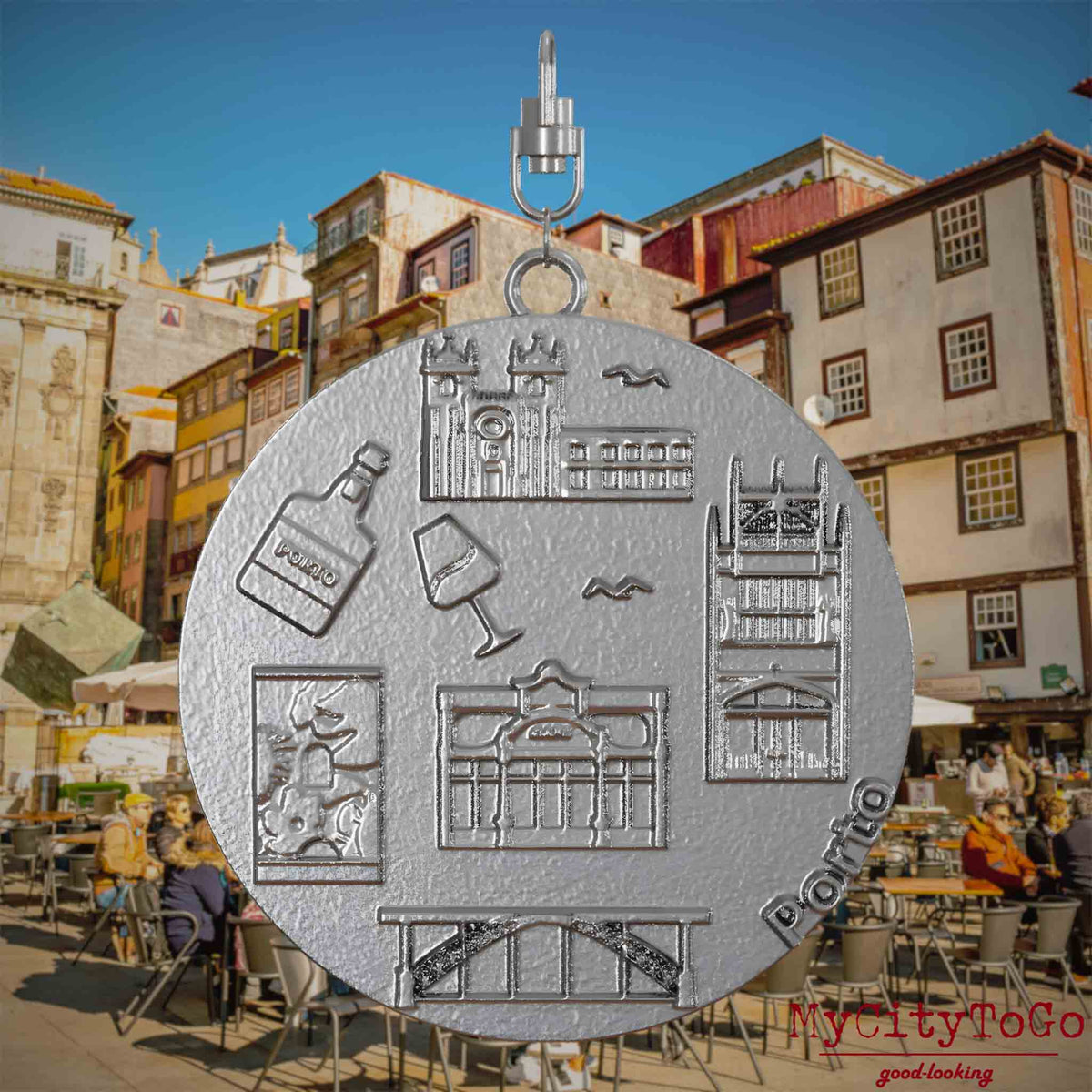 Halskette mit Drehwirbel und Rückseite eines Schmuckanhängers aus Edelstahl, auf dem Reliefs bekannter Sehenswürdigkeiten der Stadt Porto abgebildet sind. Den Hintergrund bildet eine Ansicht der Stadt Porto.
