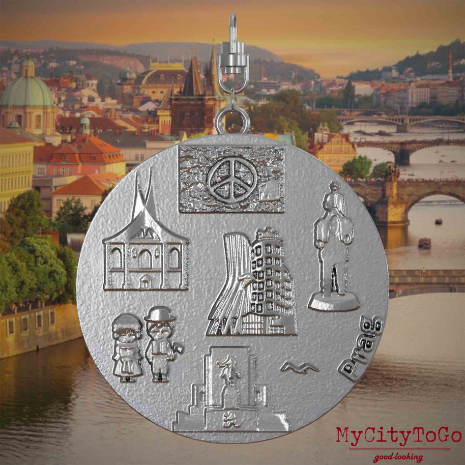 Halskette mit Drehwirbel und Rückseite eines Schmuckanhängers aus Edelstahl, auf dem Reliefs bekannter Sehenswürdigkeiten der Stadt Prag abgebildet sind. Den Hintergrund bildet eine Ansicht der Stadt Prag.
