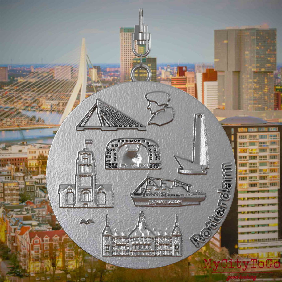 Halskette mit Drehwirbel und Rückseite eines Schmuckanhängers aus Edelstahl, auf dem Reliefs bekannter Sehenswürdigkeiten der Stadt Rotterdam abgebildet sind. Den Hintergrund bildet eine Ansicht der Stadt Rotterdam.
