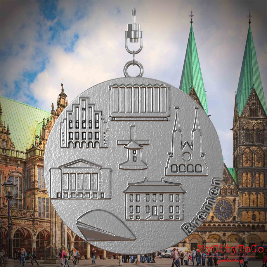 Halskette mit Drehwirbel und Rückseite eines Schmuckanhängers aus Edelstahl, auf dem Reliefs bekannter Sehenswürdigkeiten der Stadt Bremen abgebildet sind. Den Hintergrund bildet eine Ansicht der Stadt Bemen.