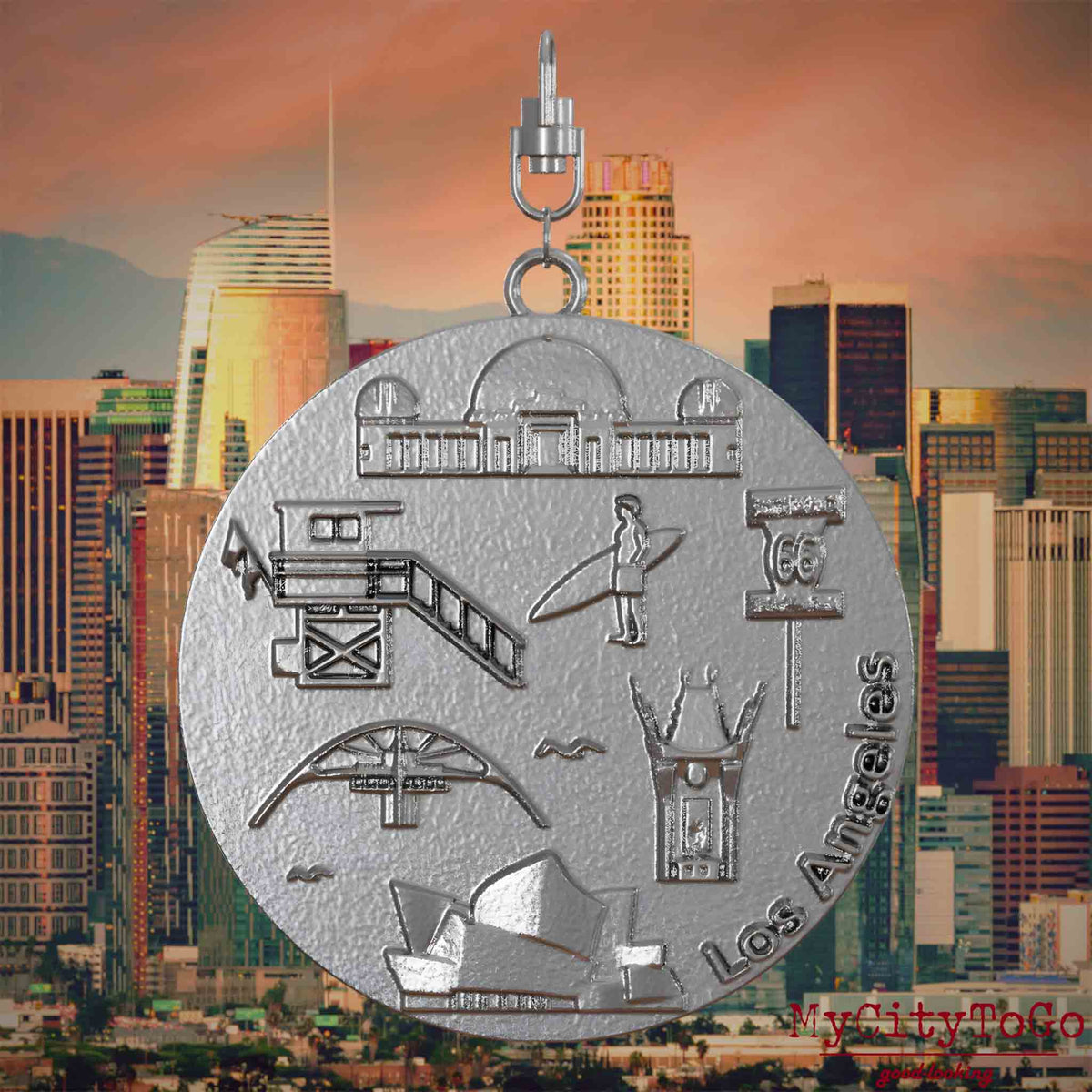 Halskette mit Drehwirbel und Rückseite eines Schmuckanhängers aus Edelstahl, auf dem Reliefs bekannter Sehenswürdigkeiten der Stadt Los Angeles abgebildet sind. Den Hintergrund bildet eine Ansicht der Angeles.

