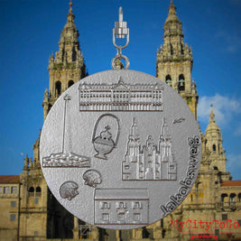 Halskette mit Drehwirbel und Rückseite eines Schmuckanhängers aus Edelstahl, auf dem Reliefs bekannter Sehenswürdigkeiten des Jakobswegs abgebildet sind. Den Hintergrund bildet eine Ansicht der Stadt Santiago de Compostela.
