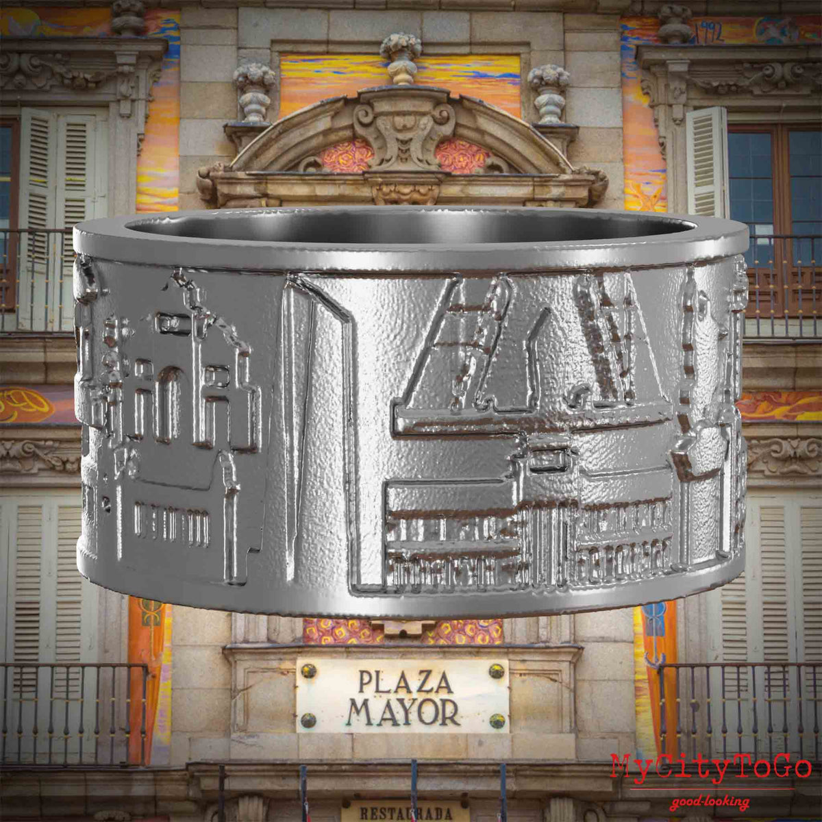 Ring aus Edelstahl mit Reliefs bekannter Sehenswürdigkeiten der Stadt Madrid. Den Hintergrund bildet eine Ansicht der Stadt Madrid.