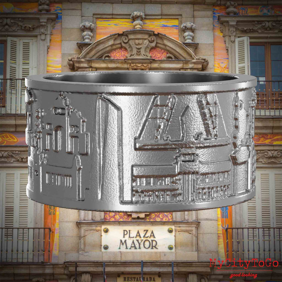 Ring aus Edelstahl mit Reliefs bekannter Sehenswürdigkeiten der Stadt Madrid. Den Hintergrund bildet eine Ansicht der Stadt Madrid.