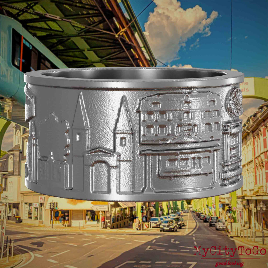 Ring aus Edelstahl mit Reliefs bekannter Sehenswürdigkeiten der Stadt Wuppertal. Den Hintergrund bildet eine Ansicht  der Stadt Wuppertal.