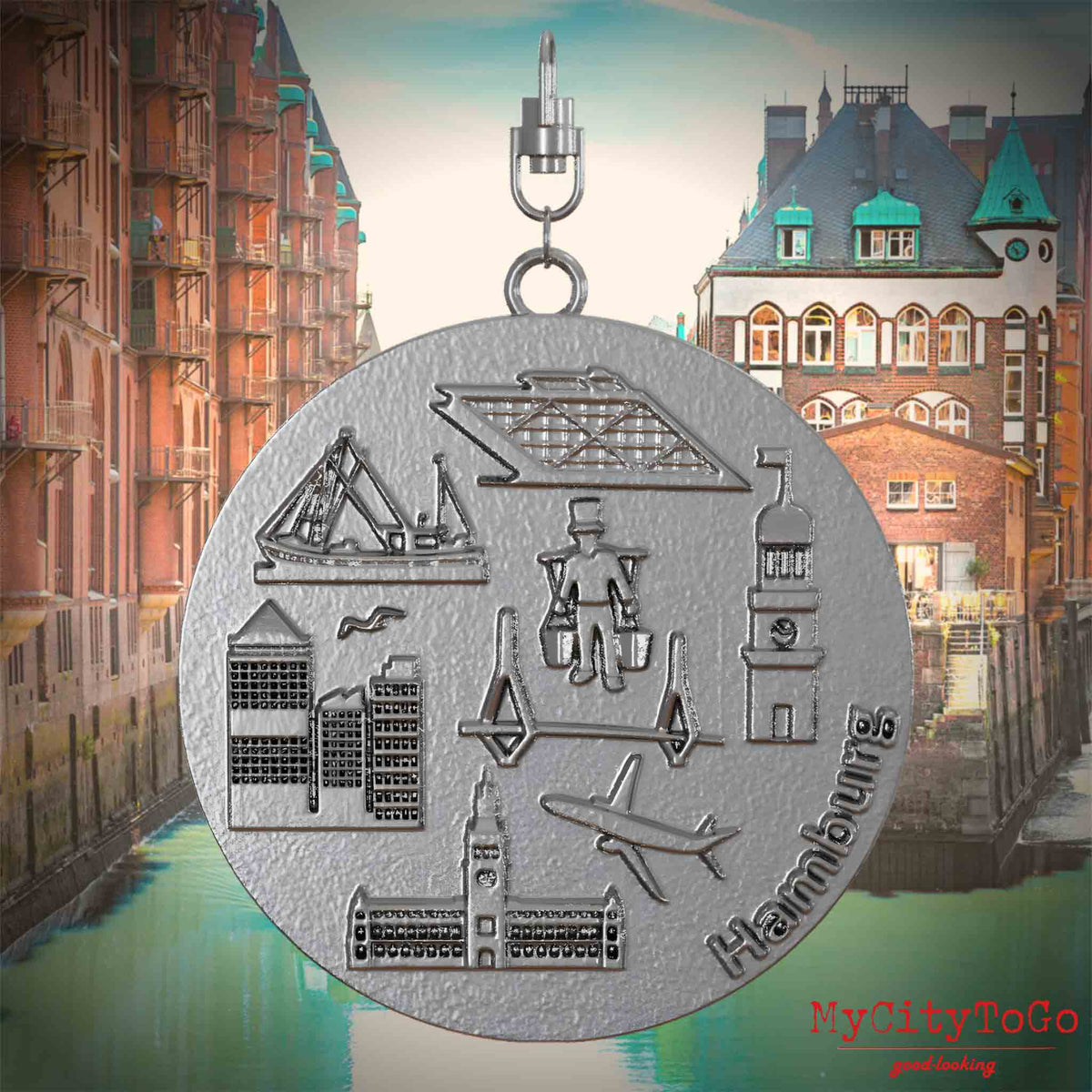 Halskette mit Drehwirbel und Vorderseite eines Schmuckanhängers aus Edelstahl, auf dem Reliefs bekannter Sehenswürdigkeiten der Stadt Hamburg abgebildet sind. Den Hintergrund bildet eine Ansicht der Stadt Hamburg.