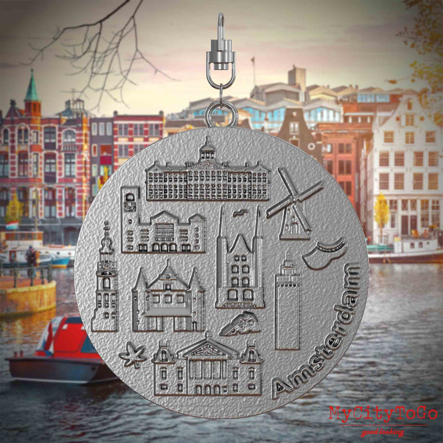 Halskette mit Drehwirbel und Rückseite eines Schmuckanhängers aus Edelstahl, auf dem Reliefs bekannter Sehenswürdigkeiten der Stadt Amsterdam abgebildet sind. Den Hintergrund bildet eine Ansicht der Stadt Amsterdam.
