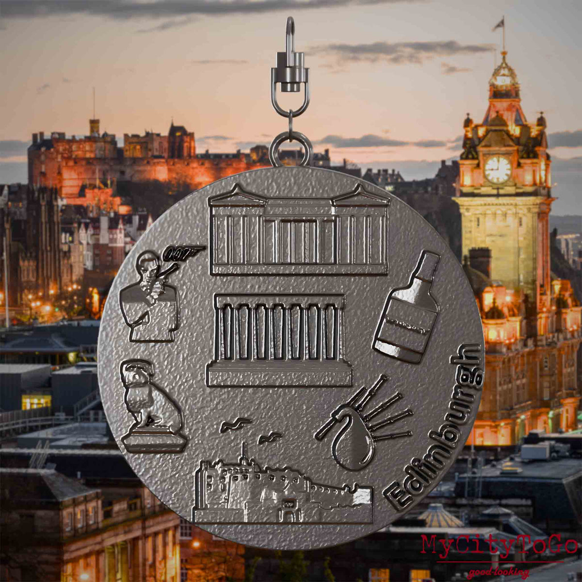 Halskette mit Drehwirbel und Vorderseite eines Schmuckanhängers aus Titan, auf dem Reliefs bekannter Sehenswürdigkeiten der Stadt Edinburgh abgebildet sind. Den Hintergrund bildet eine Ansicht der Stadt Edinburgh.
