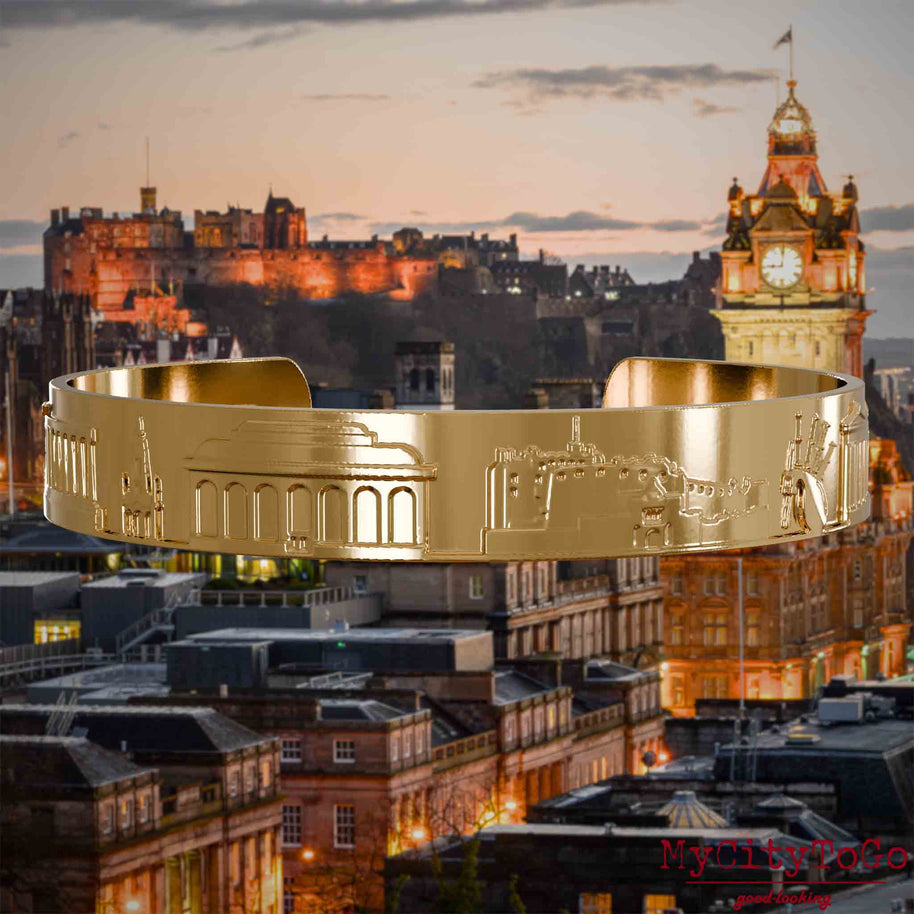 Vergoldeter Armreif mit Reliefs bekannter Sehenswürdigkeiten der Stadt Edinburgh. Den Hintergrund bildet eine Ansicht der Stadt Edinburgh.