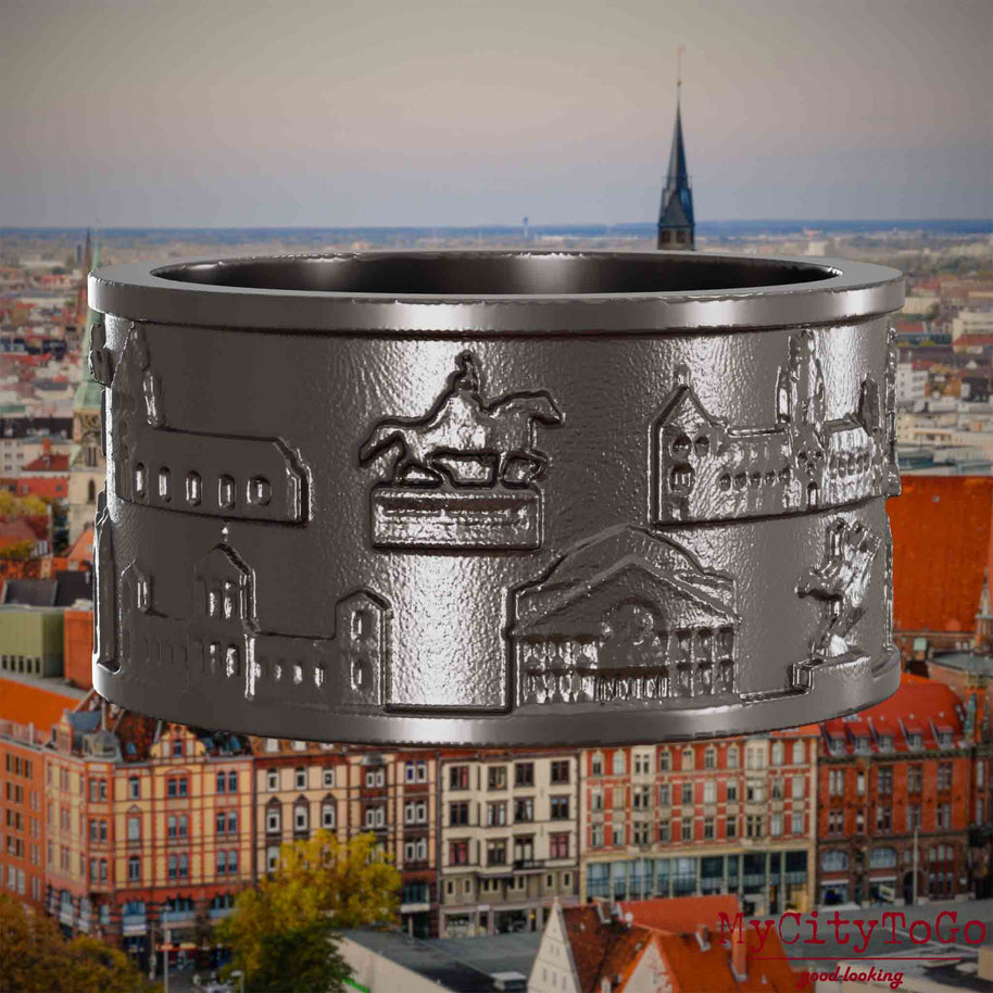 Ring aus Titan mit Reliefs bekannter Sehenswürdigkeiten der Stadt Hannover. Den Hintergrund bildet eine Ansicht der Stadt Hannover.