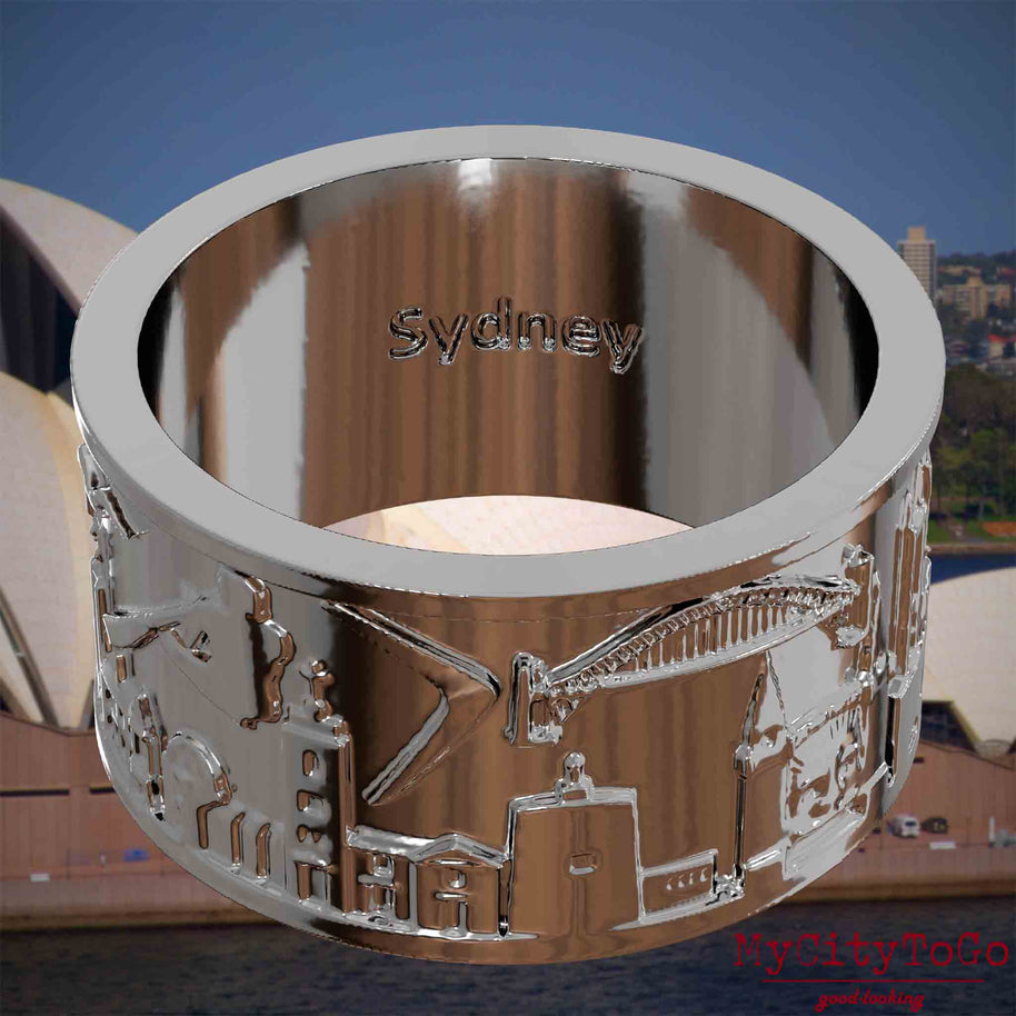 Versilberter Ring mit Reliefs bekannter Sehenswürdigkeiten der Stadt Sydney und einer Gravur des Stadtnamens auf der Innenseite. Den Hintergrund bildet eine Ansicht der Stadt Sydney.
