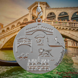 Halskette mit Drehwirbel und Vorderseite eines silbernen Schmuckanhängers, auf dem Reliefs bekannter Sehenswürdigkeiten der Stadt Venedig abgebildet sind. Den Hintergrund bildet eine Ansicht der Stadt Venedig.
