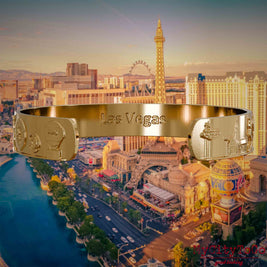Innenseite eines vergoldeten Armreifs mit Reliefs bekannter Sehenswürdigkeiten der Stadt Las Vegas und einer Gravur des Stadtnamens. Den Hintergrund bildet eine Ansicht der Stadt Las Vegas.
